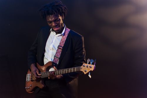 Free African American musician in a suit playing bass guitar on stage with vibrant lights. Stock Photo
