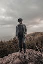 一名男子穿着休闲装，站在岩石山上，背景是多云的美景