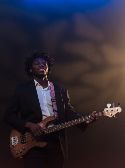 Free A smiling black musician in a suit playing an electric bass guitar on stage under dramatic lighting. Stock Photo