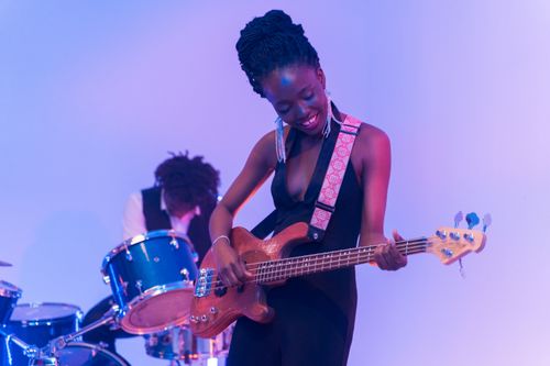 Free Confident black woman enjoying playing bass guitar on stage with band. Stock Photo