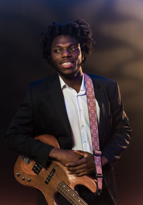 Free Elegant portrait of a musician holding a bass guitar on stage with dramatic lighting. Stock Photo