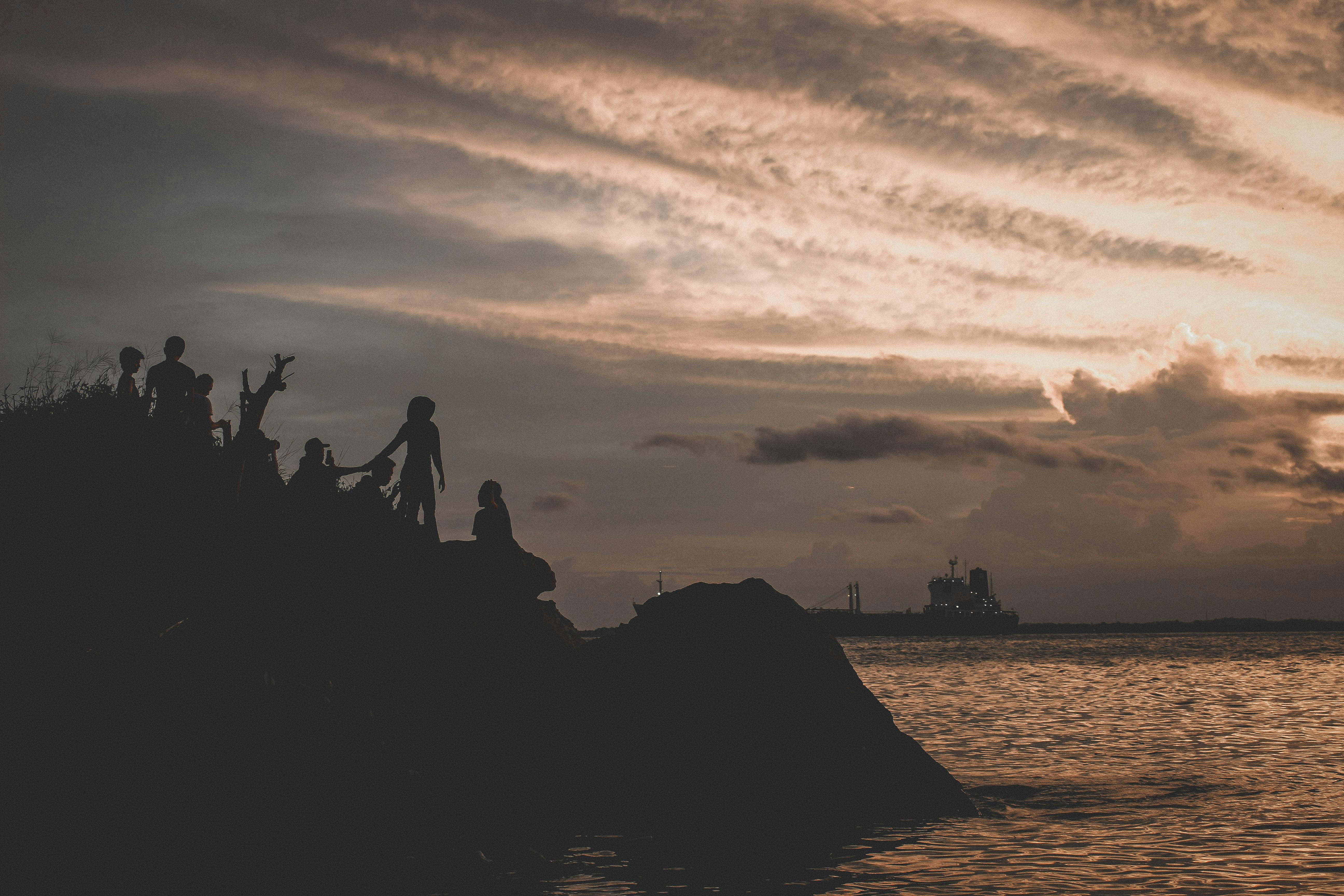 silhouette of people on mountain near body of water