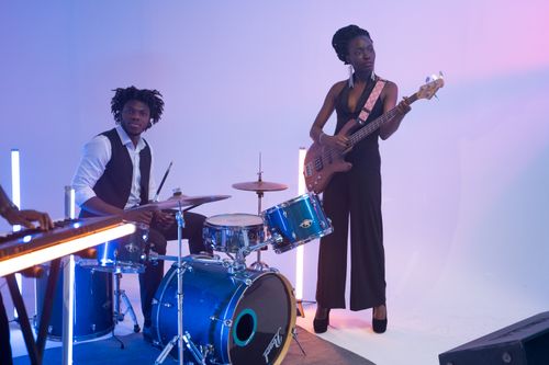 Free Energetic musicians playing drums and bass guitar under colorful stage lights. Stock Photo