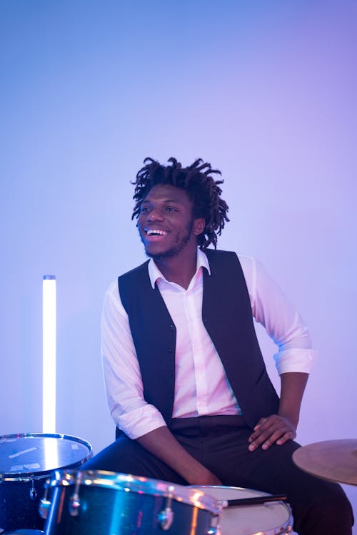 Free A Man in Black Vest Smiling while Sitting Near the Drum Set Stock Photo