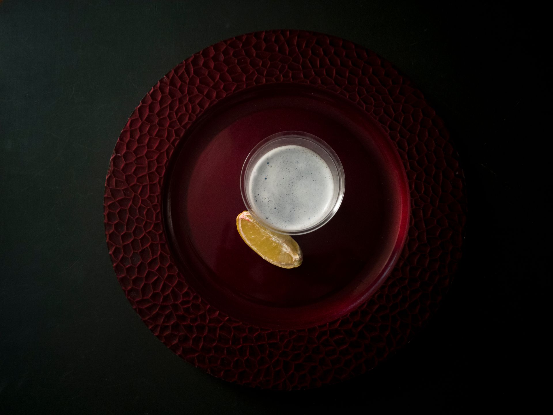 A refreshing fizzy drink garnished with lemon, served on an elegant red plate.
