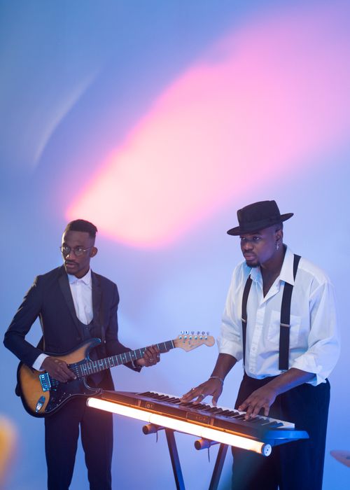 Free Black musicians performing with guitar and keyboard under vibrant lighting. Stock Photo