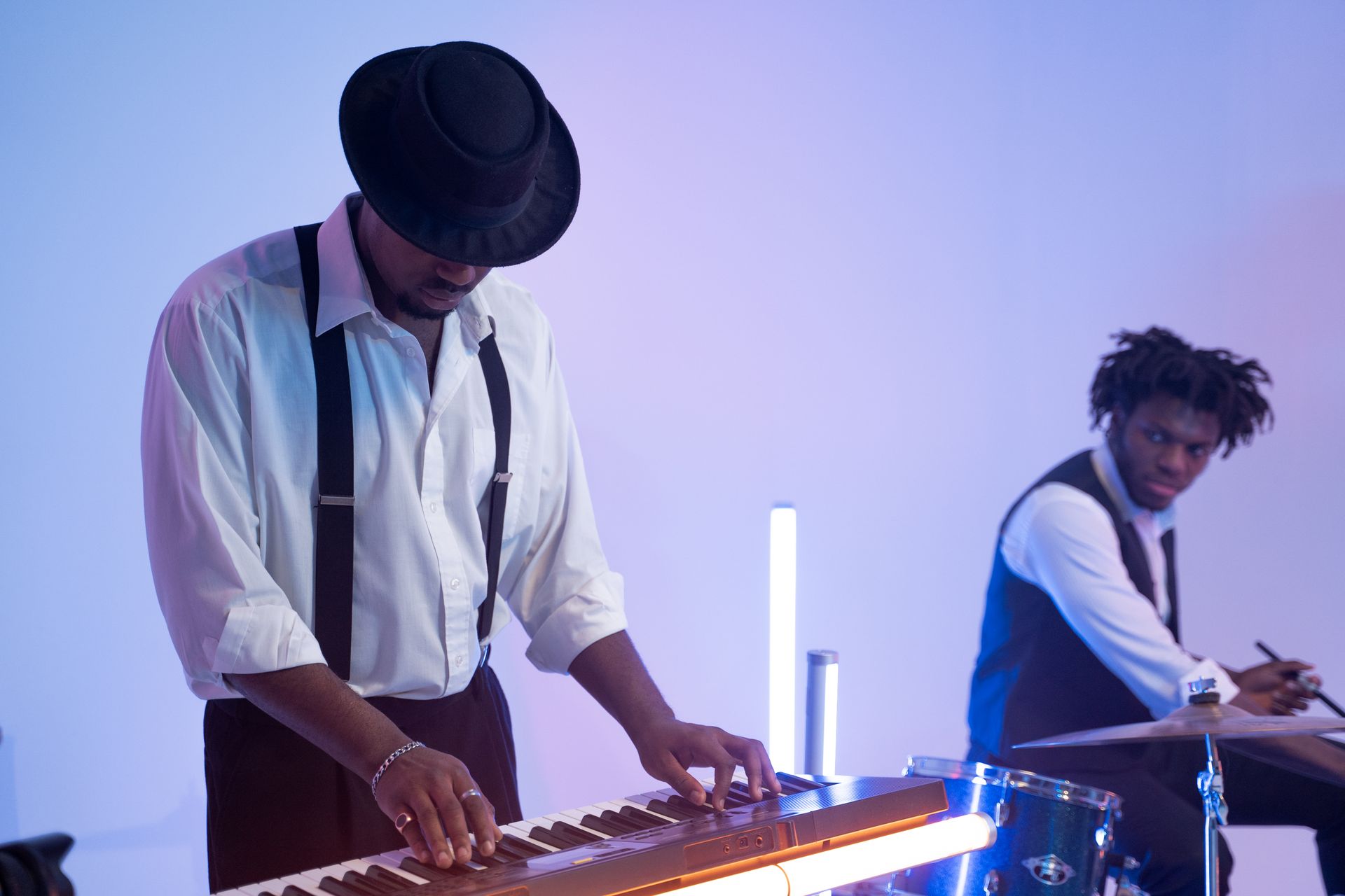 Two jazz musicians performing with keyboard and drums in a studio with blue lighting.