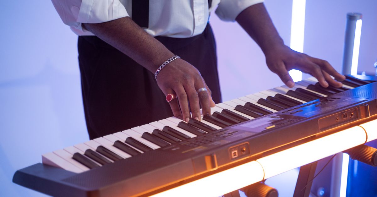 Close-up of hands on a piano keyboard next to a tablet showing an AI music interface with colorful waveform and notes