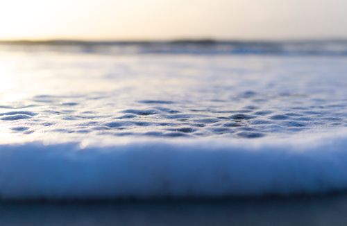Free Close-up of gentle seafoam on a tranquil beach, capturing the calm ambiance of the seaside at sunset. Stock Photo