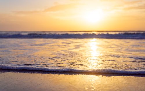 Free Serene coastal scene with golden sunrise reflecting on gentle waves at the shore. Stock Photo