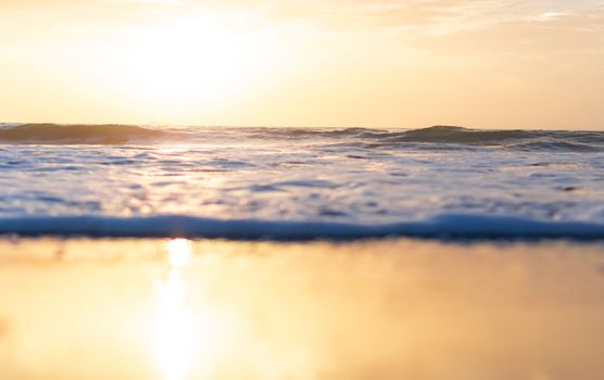 A tranquil sunrise over the ocean with gentle waves and a golden reflection on the water.