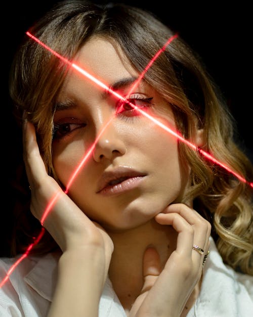 Young tender ethnic woman touching cheek and neck while looking away in laser beams on black background