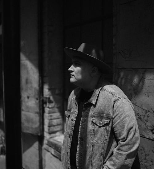 A Grayscale Photo of a Man in Denim Jacket Wearing a Hat