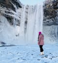 一位穿着冬装的妇女在冰岛欣赏冰冻的瀑布，凸显了它雄伟的冬季之美