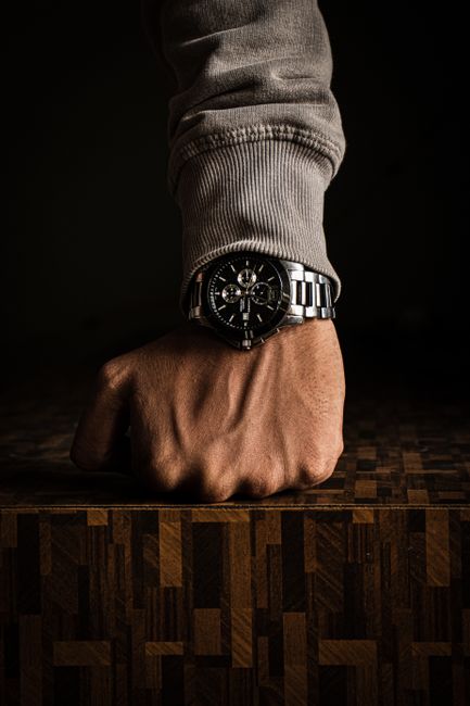 Close-up of a wristwatch on a clenched fist over a wooden table. Close-up of a wristwatch on a clenched fist over a wooden table.