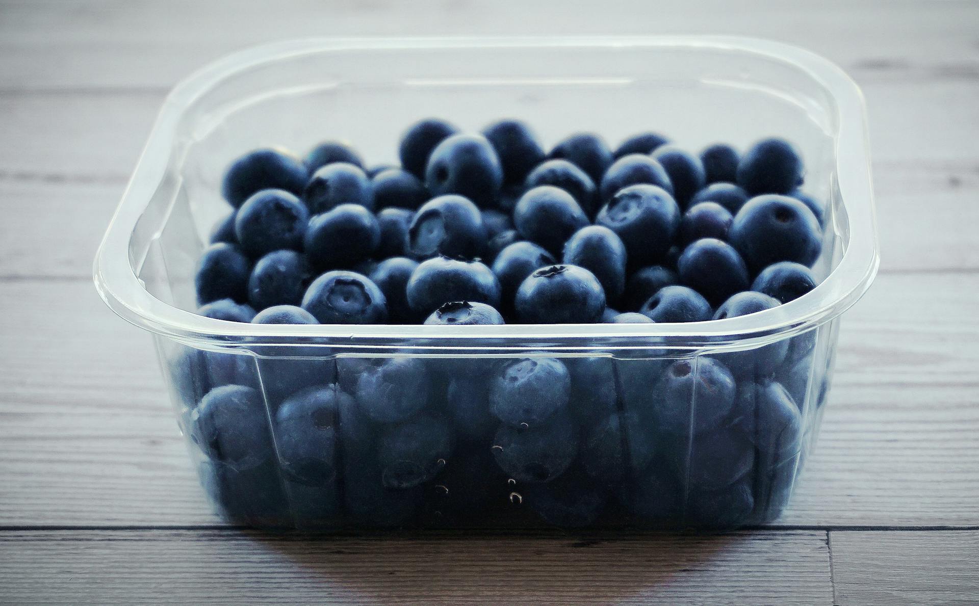 A close-up of fresh blueberries in a plastic container on a wooden table, perfect for healthy eating concepts.