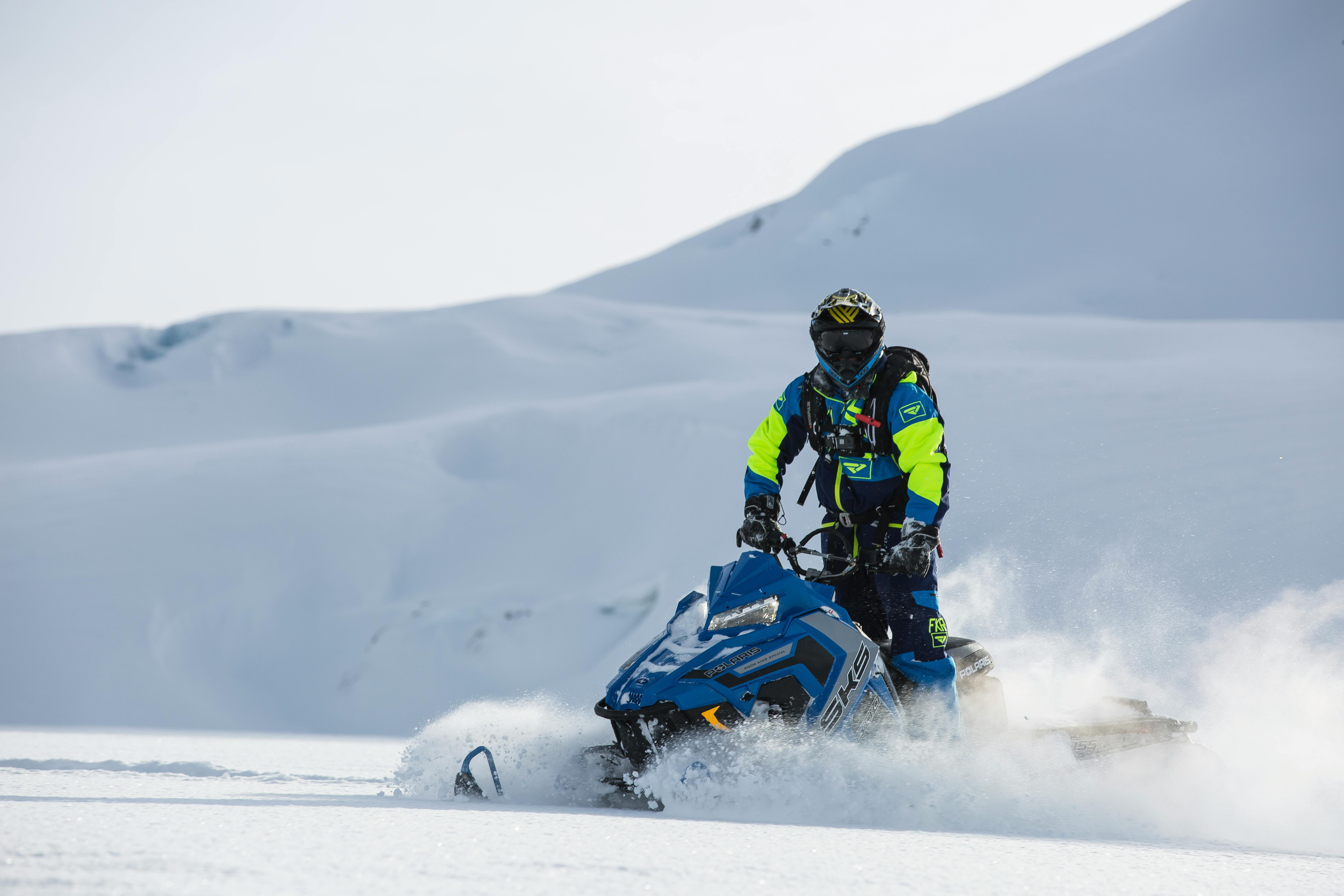 person rides on blue snowmobile at daytime