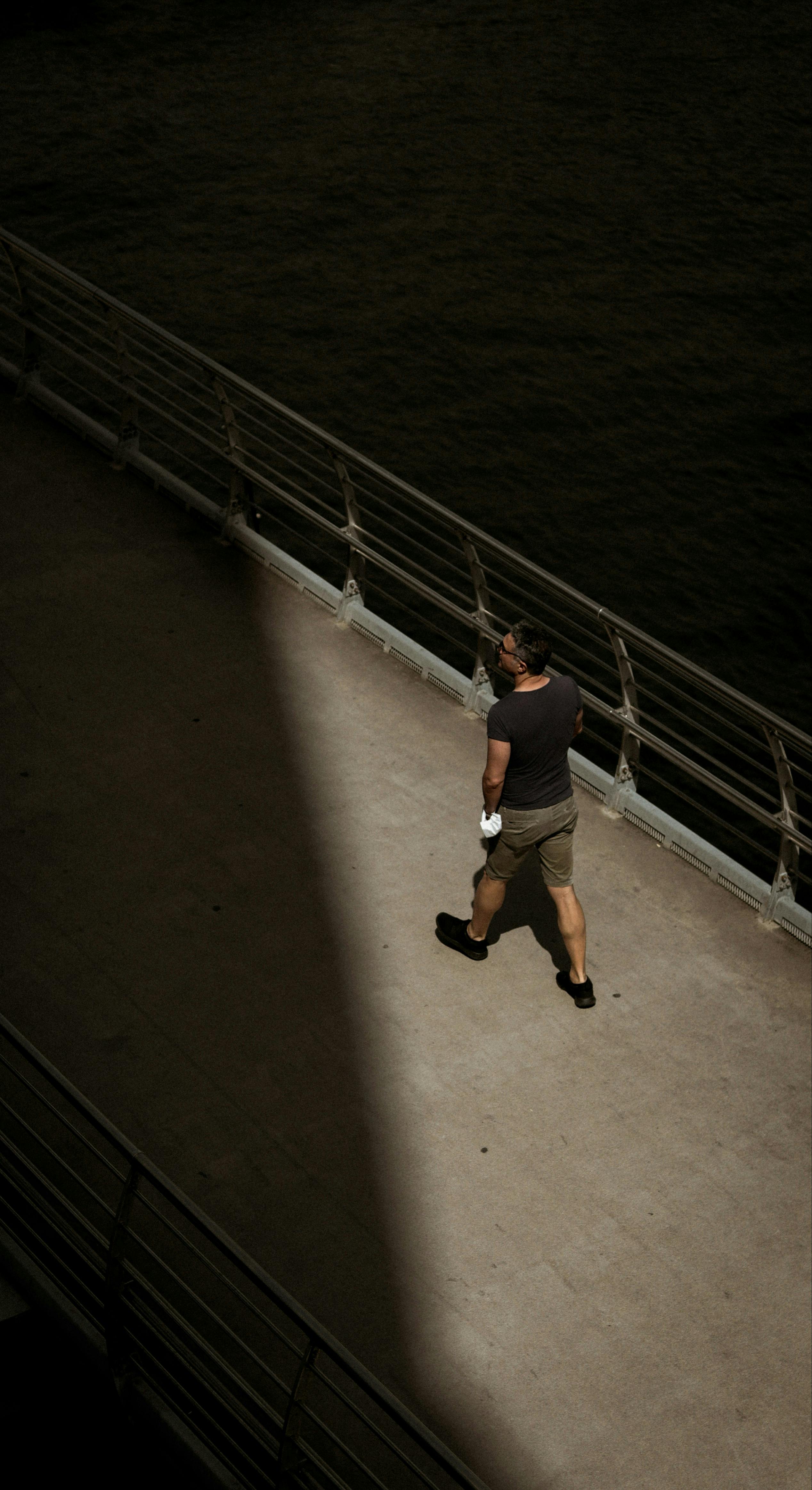 A man strolling alone on a ship deck on a sunny day, casting shadows.