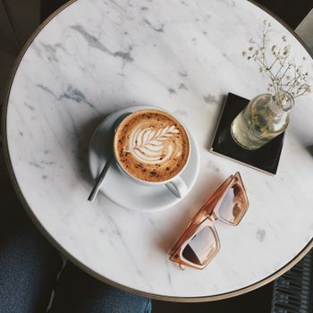 Stylish latte with delicate art and sunglasses on a marble table in Istanbul cafe, perfect for a relaxing moment.