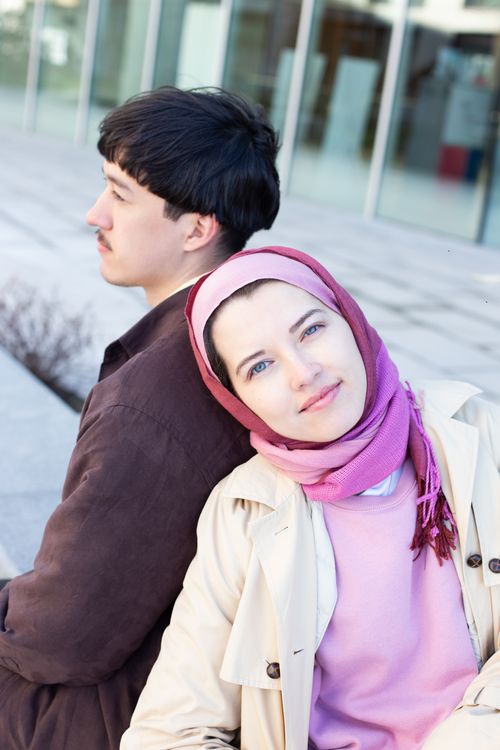 Free A couple leaning back to back, enjoying leisure time outdoors in casual outfits. Stock Photo