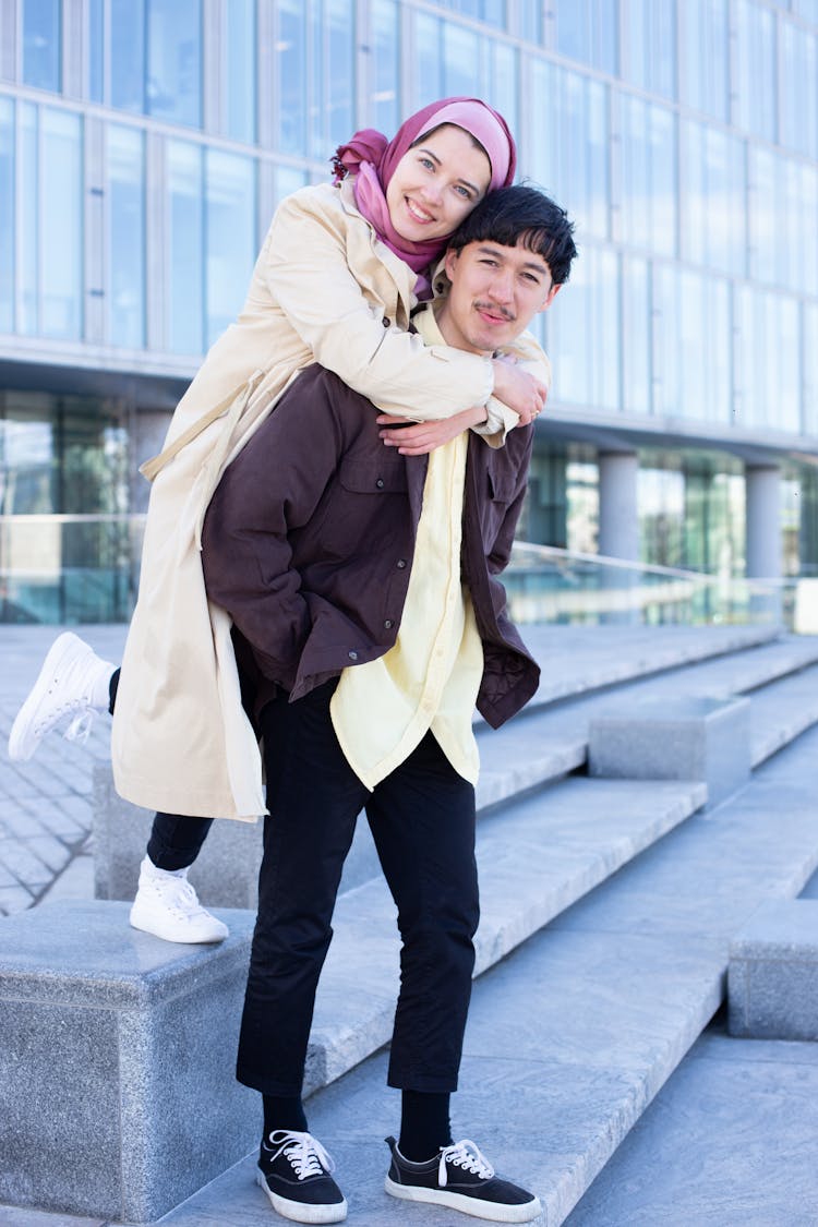 A Woman In Pink Hijab Hugging A Man From Behind Standing On Concrete Steps