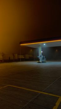 A dimly lit, isolated gas station under a foggy night sky with empty surroundings.
