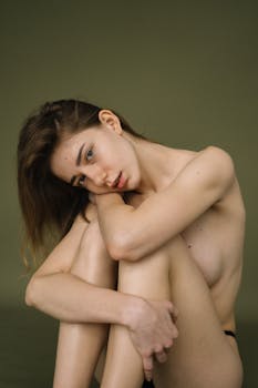 Elegant artistic nude portrait of a woman sitting against a green backdrop, exuding grace and poise.