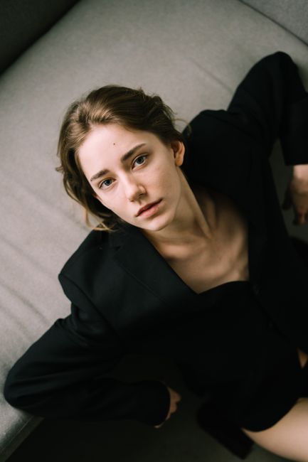 A young woman wearing a black blazer looking up in a thoughtful pose.