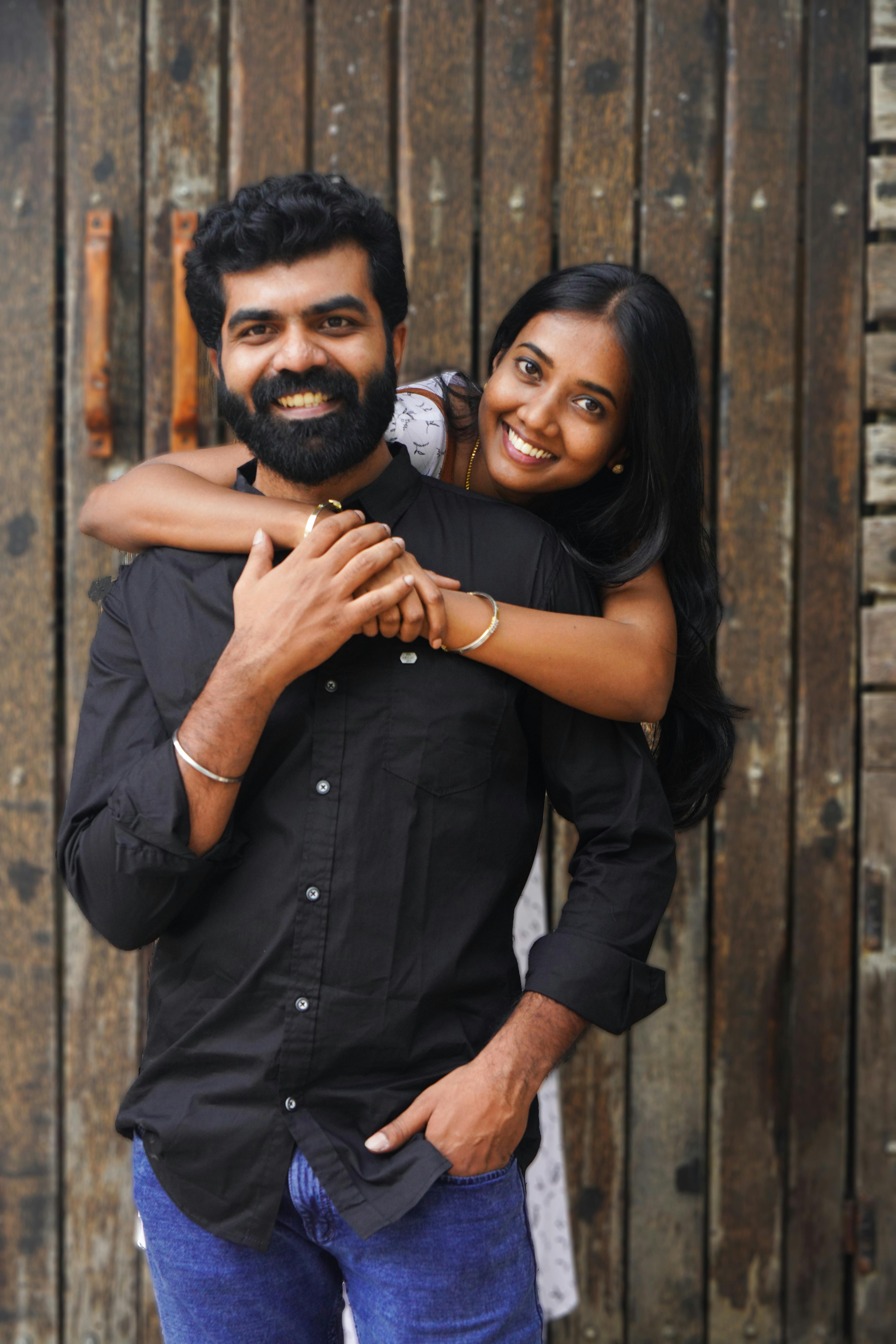 A joyful South Asian couple in a warm embrace against a rustic wooden backdrop.