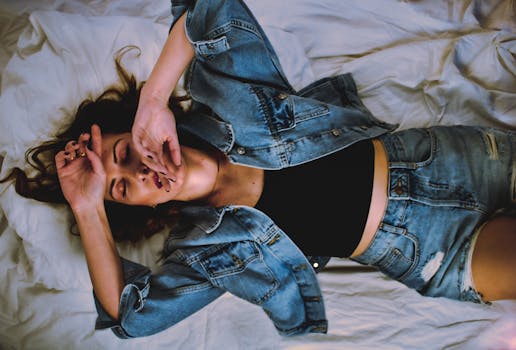 Young woman in denim resting on a bed with a relaxed posture indoors.