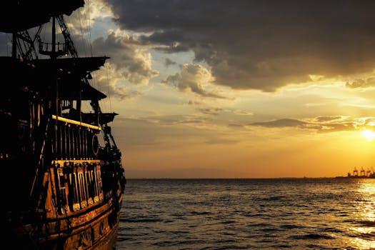 Silhouette of a pirate ship sailing into the sunset over the ocean, creating a dramatic seascape.