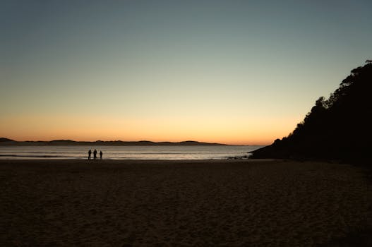 Serene morning view of a quiet NSW beach at sunrise with silhouettes against the orange horizon.