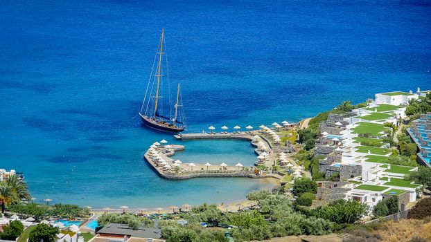 Aerial view of a luxury yacht docked at a resort with vibrant blue waters in the Mediterranean.