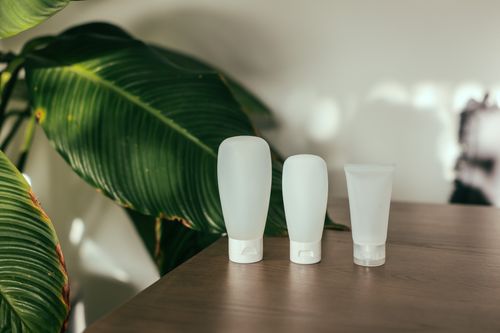 Free Three minimalist cosmetic bottles on a wooden table with large green leaves in the background. Stock Photo