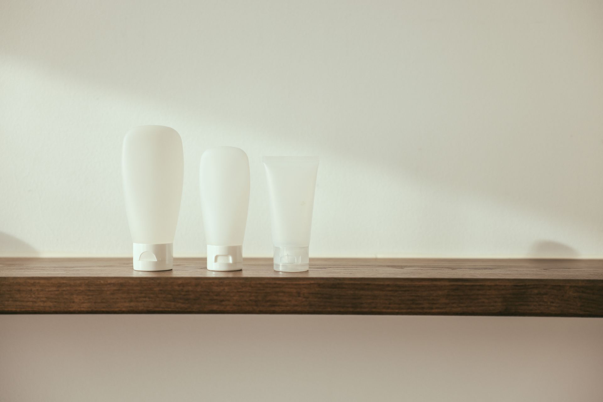 Minimalist product display with white bottles on a wooden shelf for branding mockup.