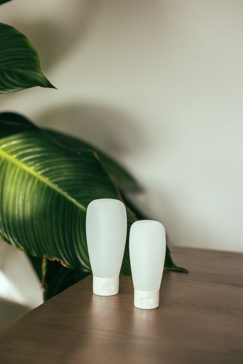 Free White cosmetic containers paired with green leaves on a wooden surface in a minimalistic setting. Stock Photo