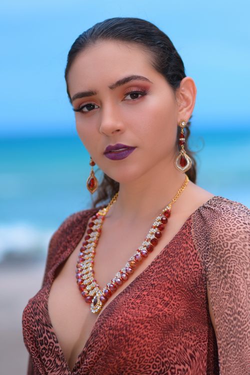 Free Woman wearing elegant jewelry standing on a tropical beach with vibrant blue ocean background. Stock Photo