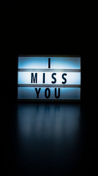A glowing lightbox displaying 'I Miss You' against a dark background, evoking feelings of longing.