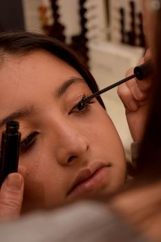 Close-up of a teenage girl applying mascara, focusing on beauty and makeup application.