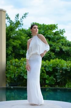A model elegantly posing in a stylish white dress outdoors by a pool.