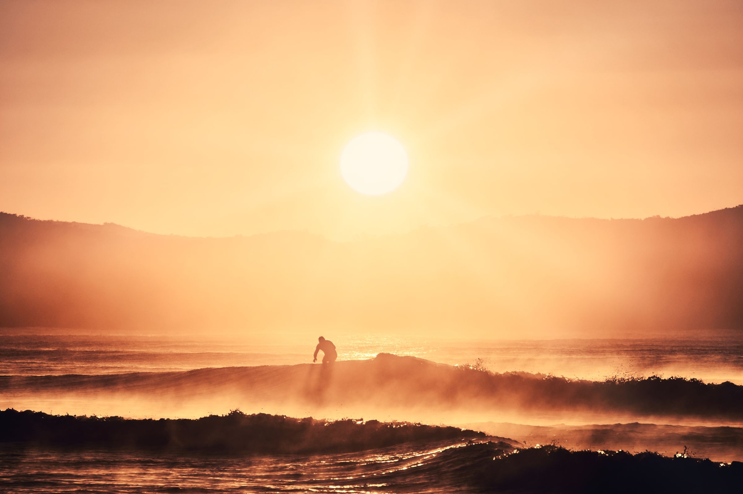 Silhouette of a surfer entering the water at sunrise