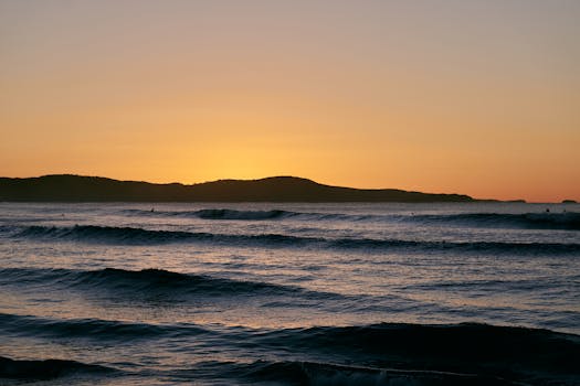 Serene sunrise over Australian ocean waves with silhouettes of distant hills, perfect for coastal tranquility.