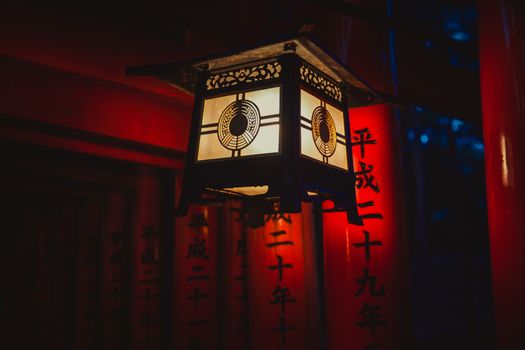 A glowing lantern at night amidst red torii gates in Fushimi Inari, Kyoto, Japan.