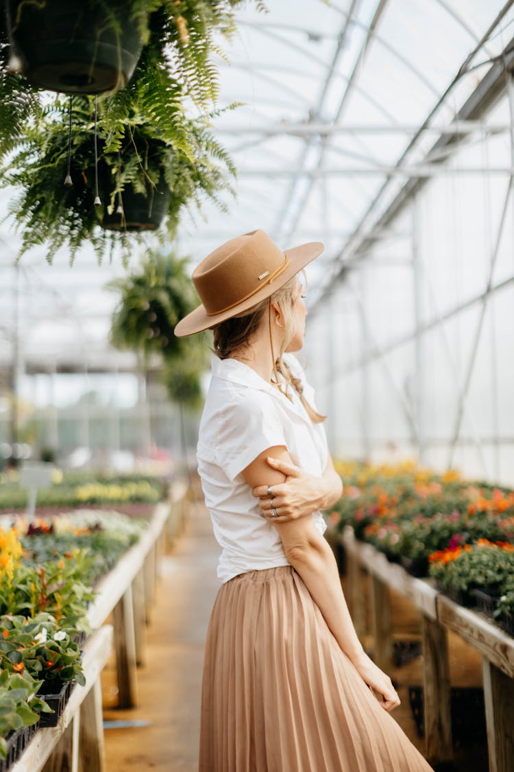 A Woman In White Shirt Standing Near The Hanging Plants