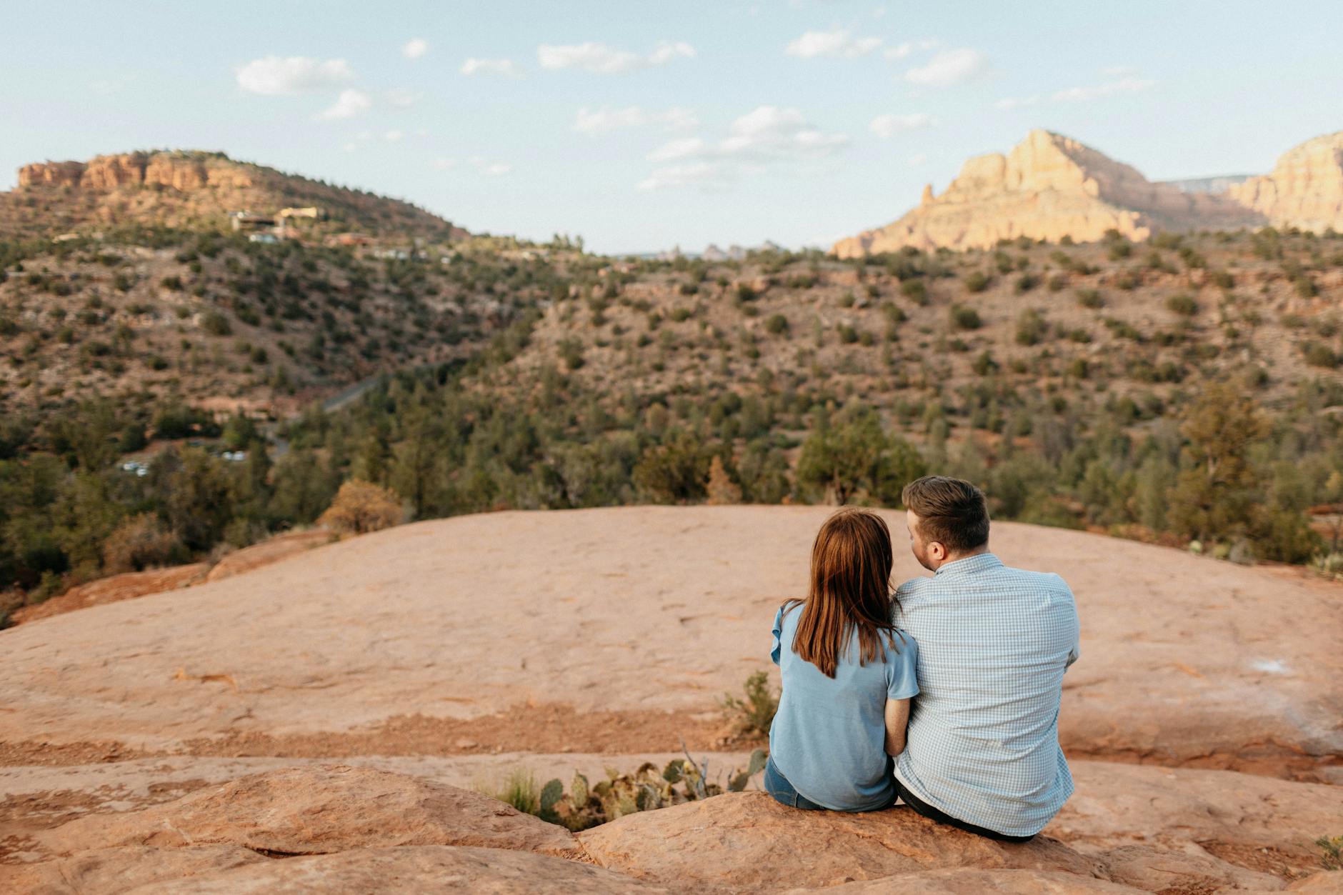 A couple sits on red rocks, enjoying a tranquil sunset in Sedona's breathtaking landscape.