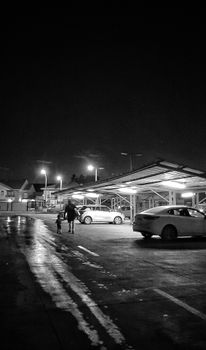 A black and white image of a parent and child walking in a parking lot at night.