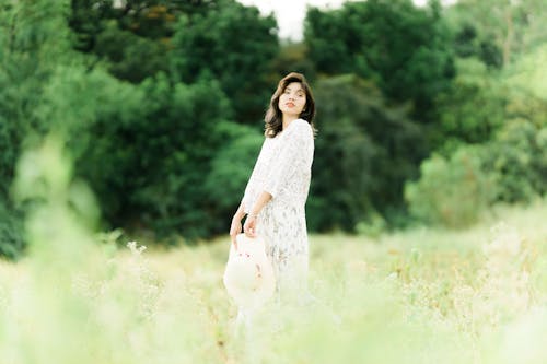 Photo of a Woman in a White Lace Dress Posing on a Grass Field