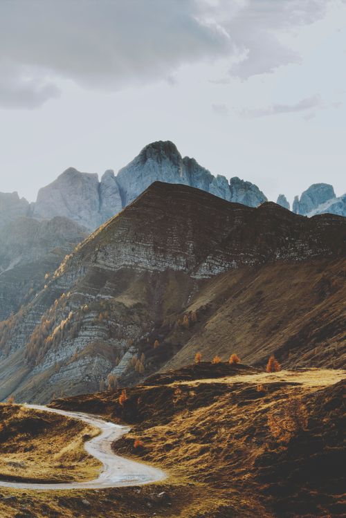 Free Stunning view of rugged mountains with a winding path under a cloudy sky. Stock Photo
