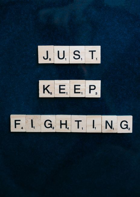 Motivational message 'Just Keep Fighting' spelled out with Scrabble tiles on a dark blue background.