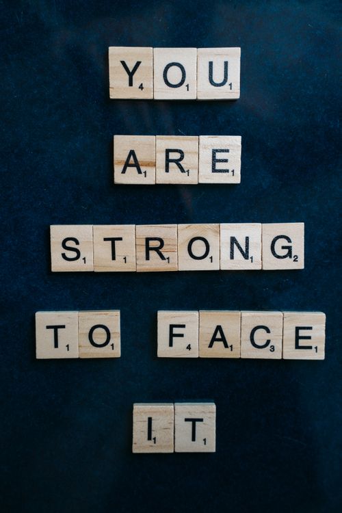 Free Wooden Scrabble tiles spell out 'You are strong to face it' on a dark surface, conveying a motivational message. Stock Photo
